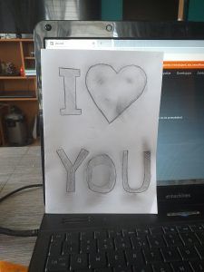 Kartka przedstawia wykonany ołówkiem napis I love you.