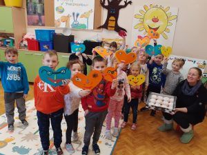 Na fotografii grupa sześciolatków prezentuje wykonane własnoręcznie kolorowe serduszka. Wychowawczyni trzyma pączki, słodki prezent z okazji Tłustego Czwartku.