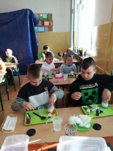 Na zdjęciu widać uczniów klas 1-3, którzy przystępują do rozpoczęcia warsztatów. Na ich ławkach przygotowane są przybory do przeprowadzenia doświadczeń. 