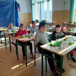 Na zdjęciu widać uczniów siedzących przy ławkach, przed nimi leżą przygotowane tace z przyborami do wykonania kosmosu w słoiczku. 