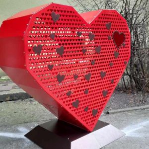 na fotografii widnieje pojemnik na zbiórkę nakrętek w kształcie czerwonego ażurowego serca 