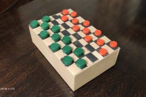 praca przedstawia planszę do gry w warcaby wykonaną z kartonu, pionkami są plastikowe nakrętki