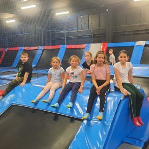 Na zdjęciu widać grupę dzieci siedzących na trampolinach