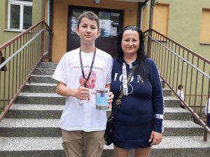 zdjęcie przestawia ucznia i jego mamę stojących przed wejściem do szkoły z puszką na datki dla chorej Ani