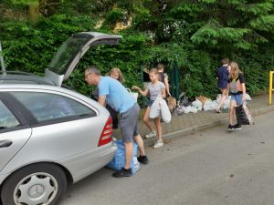 zdjęcie przedstawia rodzica i uczniów pakujących worki z nakrętkami do samochodu
