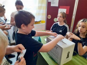 Uczeń wrzuca kartę głosowania do urny wyborczej.