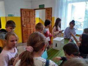 Grupa uczniów pobiera karty wyborcze od komisji.