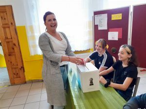 Zdjęcie przedstawia uśmiechniętą nauczycielkę oddająca swój głos w wyborach do Samorządu Uczniowskiego.