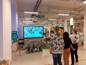 Taniec uczennic z dinozaurami na ekranie telebimu.