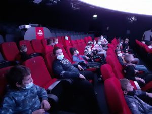 Grupa dzieci siedzi na czerwonych fotelach w sali projekcyjnej Planetarium Wenus w Zielonej Górze.
