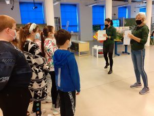 Grupa dzieci w Centrum Przyrodniczym oraz dwie panie wyjaśniające uczniom zasady zajęć warsztatowych.