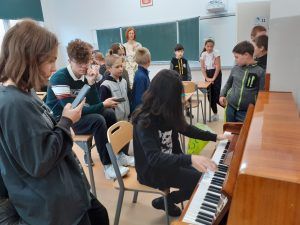 Chłopak- absolwent naszej szkoły gra na pianinie. Wokół niego stoją i słuchają występu młodsi koledzy.