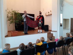 Na scenie prowadzący spotkanie i występujący muzyk demonstrują szkocki kilt - tradycyjny strój ludowy.