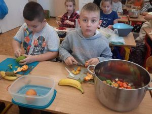 Dwóch chłopców kroi owoce do sałatki owocowej.