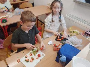 Dziewczynka z chłopcem kroją owoce do sałatki owocowej. 
