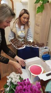 Mama, przedstawicielka Rady Rodziców i nauczycielka kładą na stole ciasto i tort.