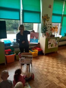 Bibliotekarka pokazuje dzieciom plakat akcji "Mała książka Wielki człowiek".