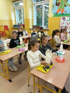 Na zdjęciu uczennice klas drugiej i trzeciej wykonują doświadczenie z gumową rękawicą