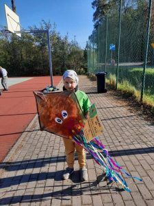 Na zdjęciu stoi przedszkolak w rękach trzyma dyplom oraz swój latawiec