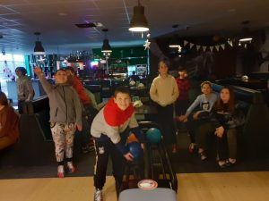 Fotografia 4 przedstawia chłopców obserwujących wyniki na tablicy i uśmiechniętego chłopca biorącego kulę z podajnika.