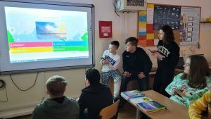 zdjęcie przedstawia grupę uczniów rozwiązujących zadania przed tablicą interaktywną