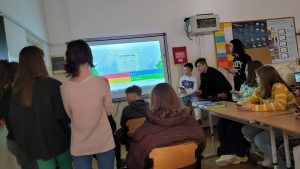 zdjęcie przedstawia grupę uczniów rozwiązujących zadania przed tablicą interaktywną