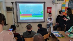 zdjęcie przedstawia grupę uczniów rozwiązujących zadania przed tablicą interaktywną