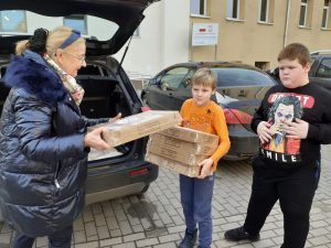 na zdjęciu kobieta przekazująca pączki dwojgu uczniów