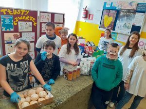 grupa uśmiechniętych uczniów i wolontariuszy przy stole z darami dla schroniska