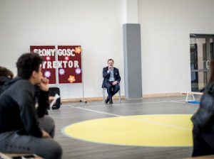 na tle dekoracyjnej tablicy dyrektor szkoły i uczniowie zadający pytania