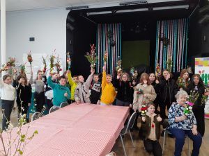 grupa uczniów z seniorką , która uczyła ich robienia palm trzymający zrobione palmy