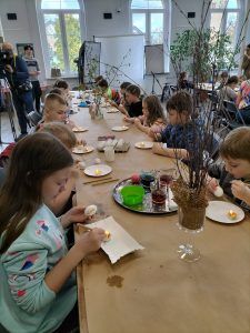 dzieci przy stołach ozdabiają jajka
