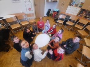 na zdjęciu dzieci siedzą w kole i przygotowują pracę plastyczną