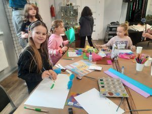 przy stole siedzą dziewczynki, pracujące nad swoimi dziełami