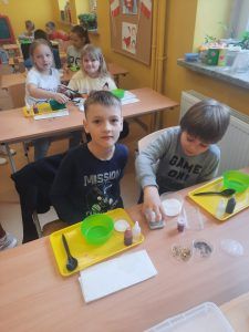 uczniowie przy stolikach odmierzają składniki