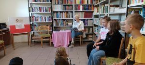 grupa uczniów słucha czytanej książki przez gościa biblioteki