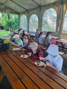 uczniowie pod namiotem jedzą kiełbaski z grilla