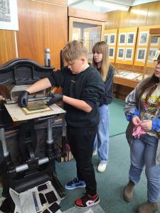 Uczniowie uczestniczą w warsztatach graficznych z wykorzystaniem prasy introligatorskiej do złoceń