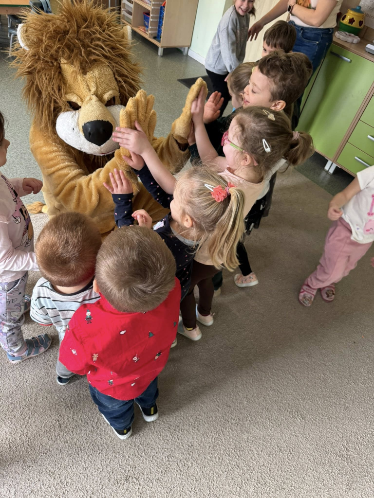 Grupa uśmiechniętych dzieci przybija piątkę mężczyźnie przebranym za lwa.