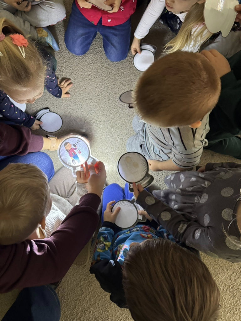 Grupa dzieci odczytuje wylosowaną wróżbę, oświetlając ją światłem latarki.