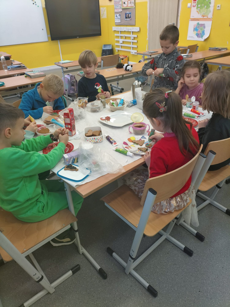 Grupa dzieci siedzi przy wspólnym stole i ręcznie dekoruje pierniczki.