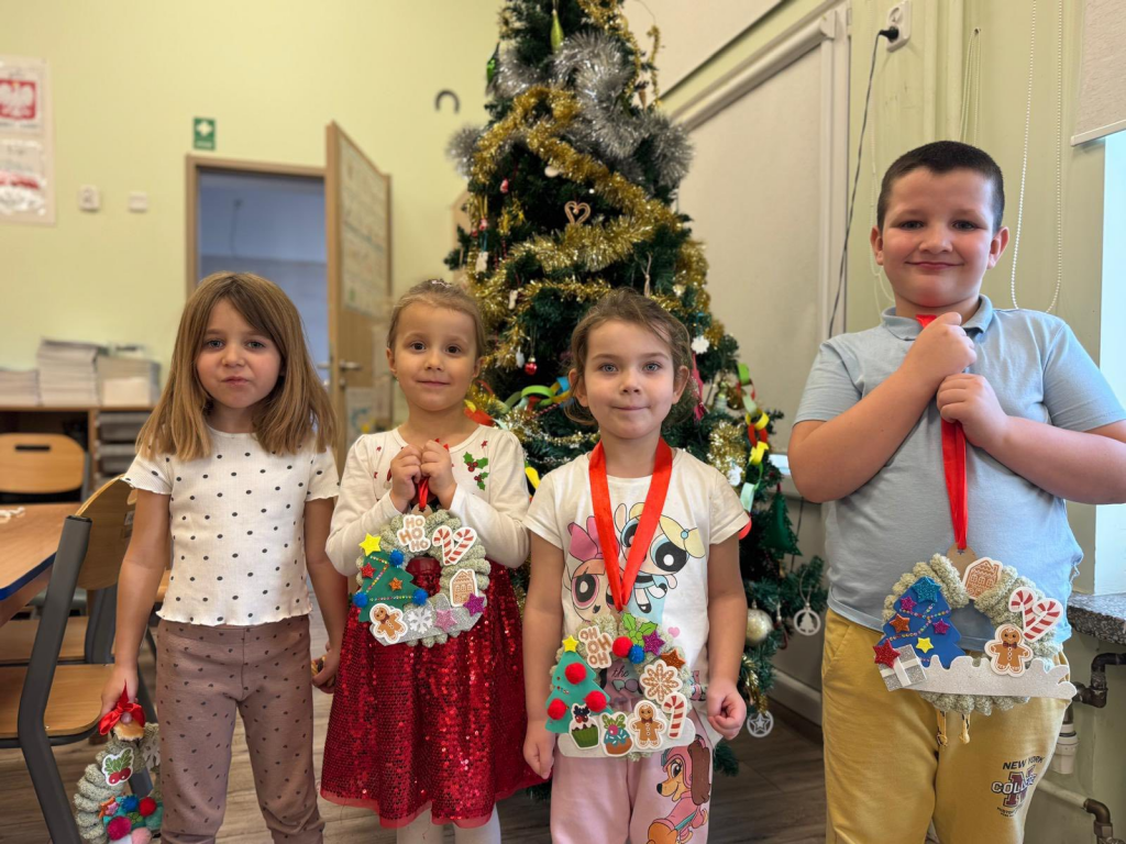 Dzieci stoją przed choinką z wieńcami, które samodzielnie przygotowały wspólnie z rodzicami.