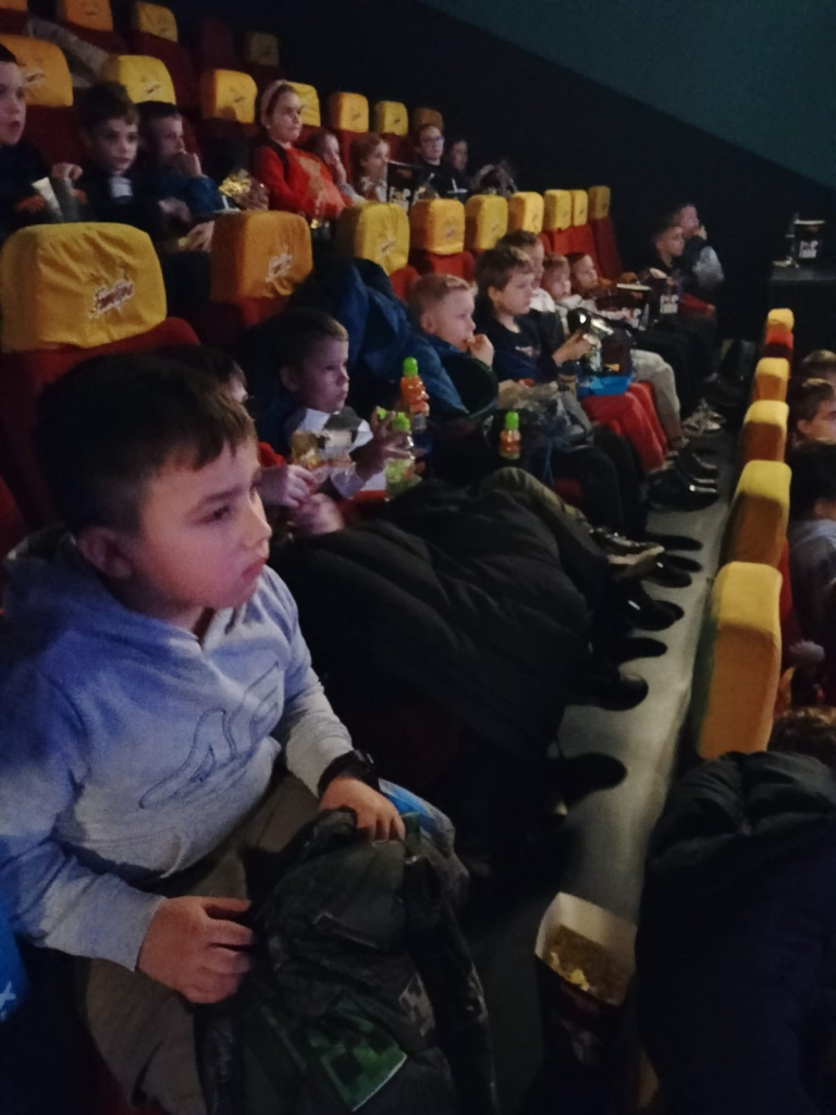 Dzieci siedzą w kinowej sali, oglądając film i trzymając przekąski.