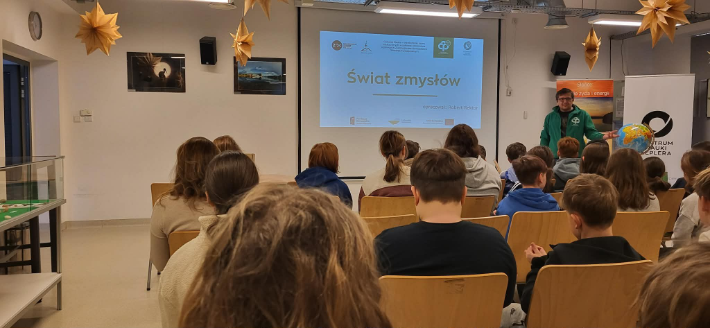 Grupa dzieci siedzi przodem do tablicy na której wyświetlony jest temat prezentacji ,,Świat zmysłów"