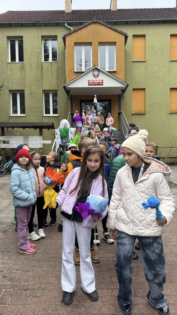 Grupa uczniów ustawia się w pary, by wspólnie wyruszyć przywitać wiosnę. Na pierwszym planie dwie dziewczynki trzymają w rękach marzanny.