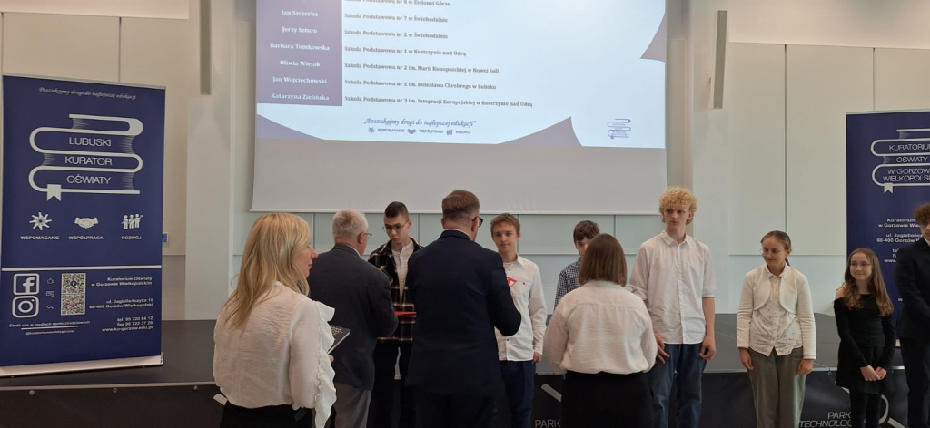 Uczniowie odbierają dyplomy i gratulacje za zdobycie tytułu laureata wojewódzkiego konkursu języka angielskiego.